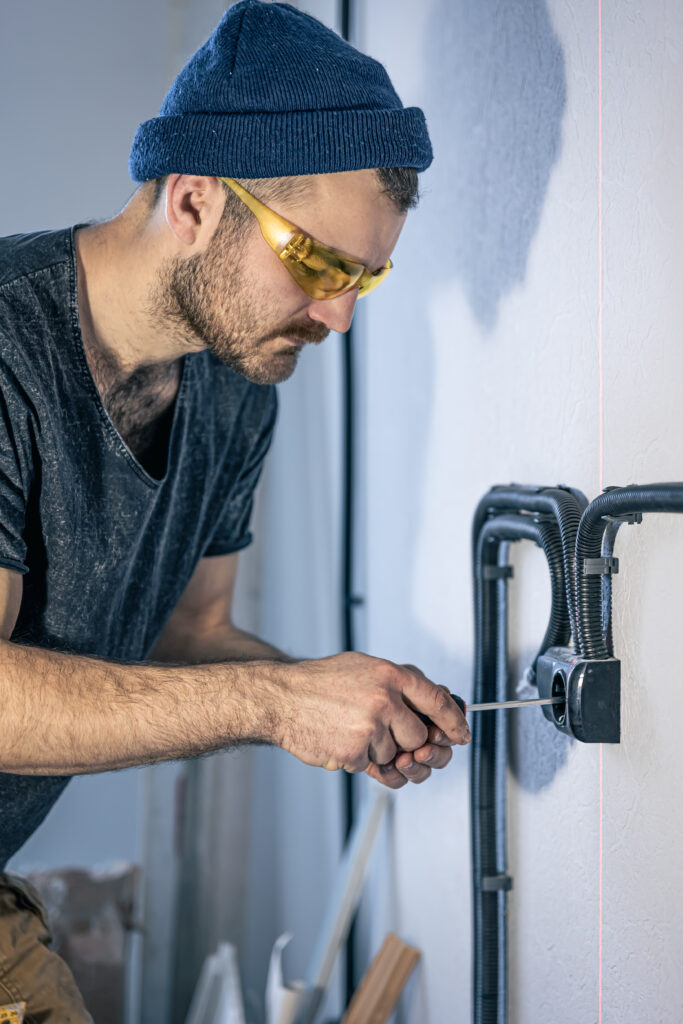 An Electrician Is Mounting Electric Sockets On The White Wall Indoors.